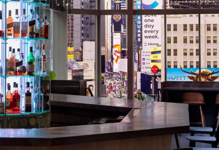 M Social Times Square gay-friendly hotel bar view. Colorful Times Square billboards seen through the window. LGBT travel advice.