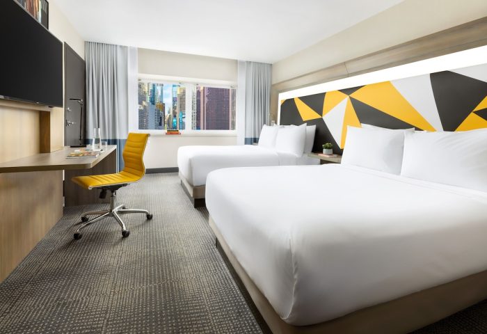 M Social Times Square hotel room with two beds, desk, yellow chair, and city view. Gay-friendly hotel for gay men travelers.