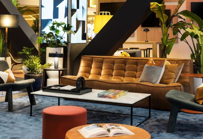 M Social Times Square gay-friendly hotel lounge. Modern interior with brown leather sofa, chairs, tables, plants. Stylish, welcoming space.