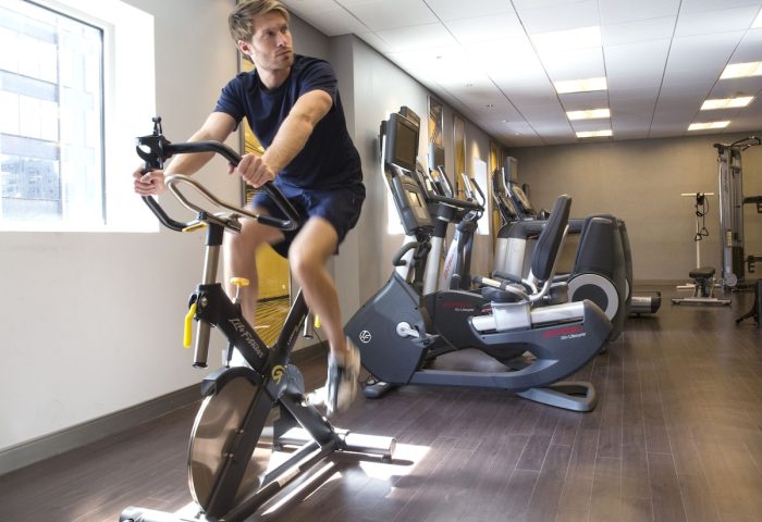 Gay-friendly M Social Times Square hotel gym. Man on exercise bike. Great for gay men's travel advice. Stay fit on vacation.