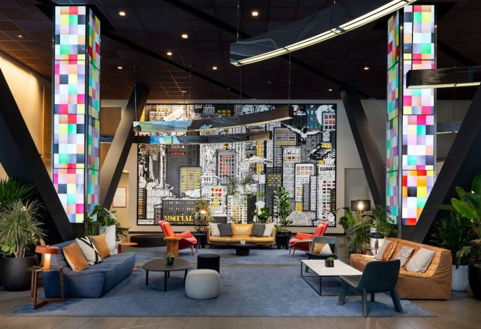M Social Times Square lobby. Gay-friendly hotel interior with colorful columns, NYC mural art, and modern seating for guests.