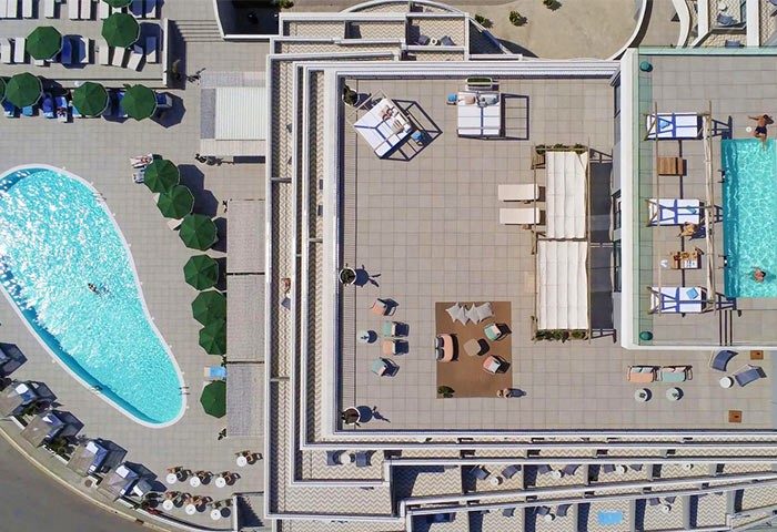 Aerial view of ME Sitges Terramar, a gay-friendly, pet-friendly hotel. Pools, lounge areas, and umbrellas create a relaxing atmosphere.