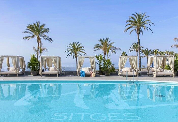 ME Sitges Terramar gay-friendly hotel pool view. Cabanas line the pool with palm trees. A pet-friendly hotel for gay travel in Sitges.