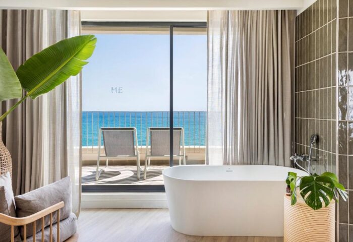 ME Sitges Terramar gay-friendly hotel bathroom with ocean view. Pet-friendly hotel room with tub, chairs on balcony, and modern design.