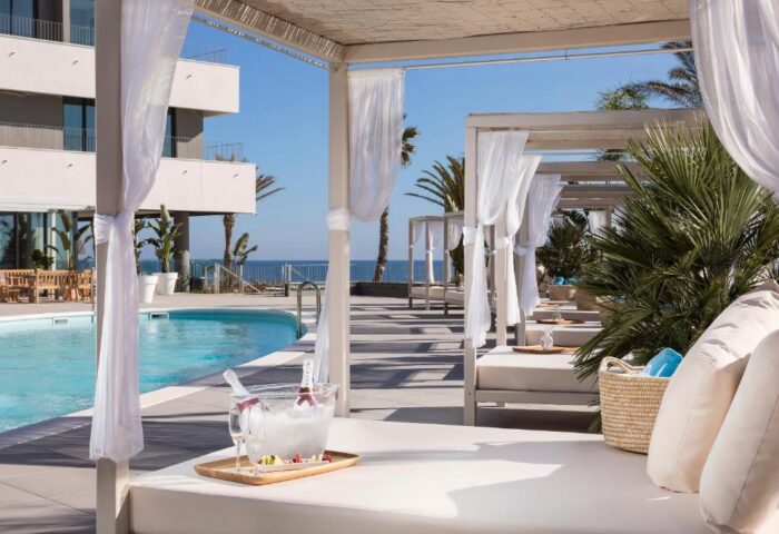 ME Sitges Terramar gay-friendly hotel pool view. Cabanas with white curtains, champagne bucket, and ocean backdrop. Pet-friendly resort.