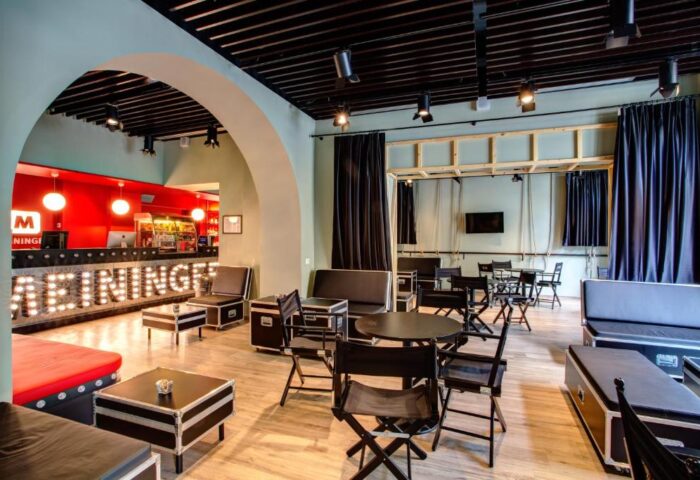 MEININGER Roma Termini gay-friendly hotel lounge area. Modern design with black furniture, wooden floors, and a red reception desk. Comfortable seating.
