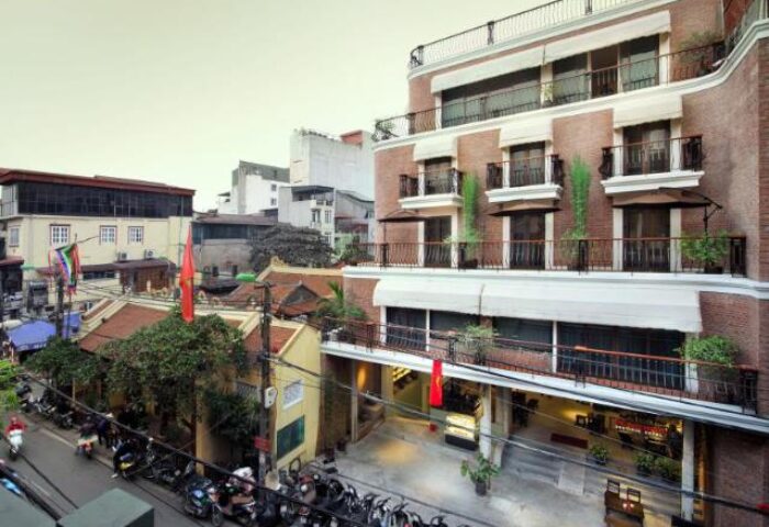 MK Premier Boutique Hotel, a gay-friendly hotel. Exterior view of the hotel with balconies, awnings, and Vietnamese flags. Hanoi, Vietnam.