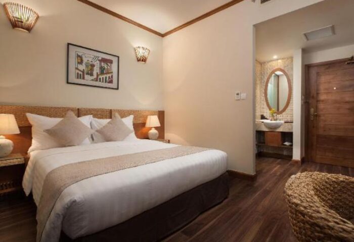 MK Premier Boutique Hotel room. Gay-friendly hotel with bed, bathroom, wood floors, lamps, art, and woven chair. Ideal for gay men travel.