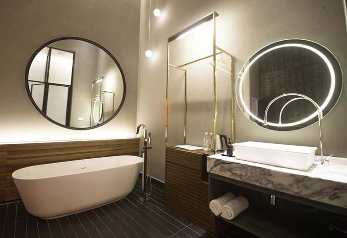 MOV Hotel gay-friendly room. Modern bathroom with tub, round mirrors, marble sink, and gold accents. Upscale design for gay travelers.