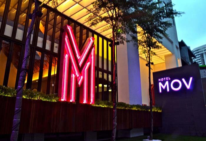 MOV Hotel facade with neon 'M' and hotel signage. Gay-friendly hotel with modern design, perfect for gay men travel. Night view.