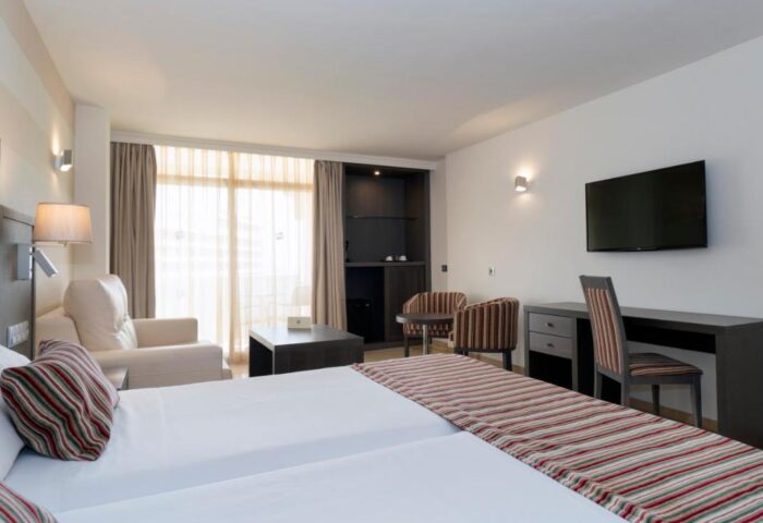 MS Aguamarina Suites gay-friendly hotel room. Modern interior with twin beds, desk, TV, seating area, and balcony. Comfortable stay.