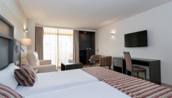 MS Aguamarina Suites gay-friendly hotel room. Modern interior with twin beds, desk, TV, seating area, and balcony. Comfortable stay.