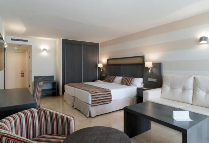 MS Aguamarina Suites gay-friendly hotel room. Double bed, sofa, desk, and striped chair in a modern, well-lit suite. Comfy gay travel.