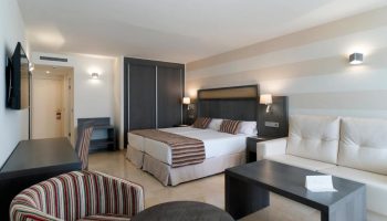 MS Aguamarina Suites gay-friendly hotel room. Double bed, sofa, desk, and striped chair in a modern, well-lit suite. Comfy gay travel.