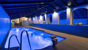 Indoor pool at MS Aguamarina Suites, gay-friendly hotel. Blue lighting, waterfall feature, and tiled walls create a relaxing atmosphere.