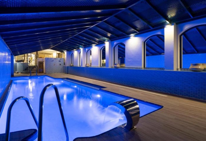 Indoor pool at MS Aguamarina Suites, gay-friendly hotel. Blue lighting, waterfall feature, and tiled walls create a relaxing atmosphere.