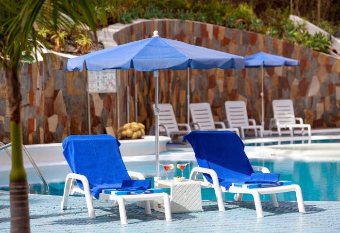 MUR Aparthotel Buenos Aires, Gran Canaria pool. Gay-friendly hotel with blue umbrellas, lounge chairs, and cocktails. Relaxing vacation.