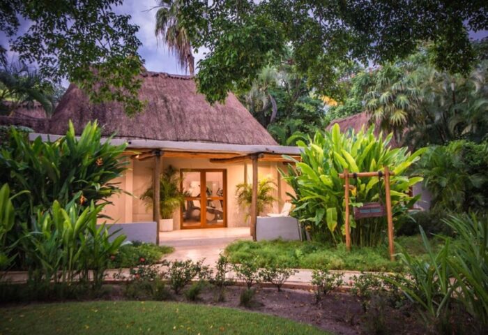 Mahekal Beach Front Resort and Spa gym. Gay-friendly hotel with thatched roof, lush greenery, and exercise equipment visible through glass doors.