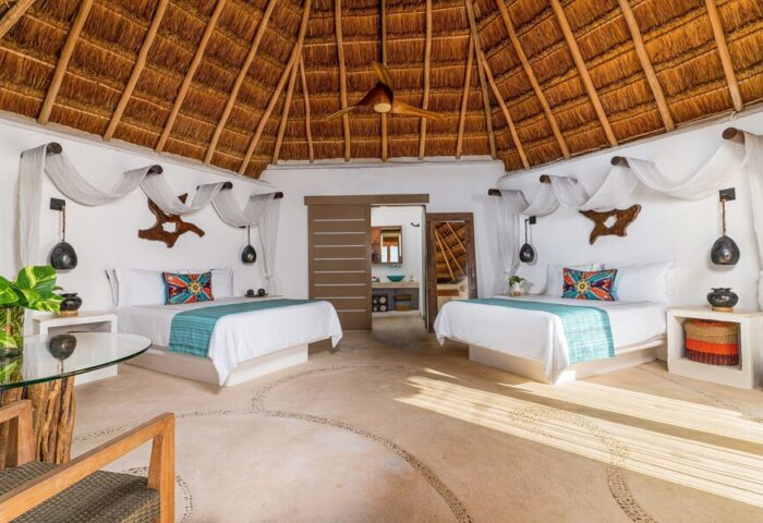 Mahekal Beach Front Resort & Spa gay-friendly hotel room. Two beds, thatched roof, & rustic decor. Ideal for gay travel & relaxation.