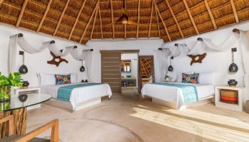 Mahekal Beach Front Resort & Spa gay-friendly hotel room. Two beds, thatched roof, & rustic decor. Ideal for gay travel & relaxation.