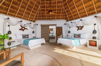 Mahekal Beach Front Resort & Spa gay-friendly hotel room. Two beds, thatched roof, & rustic decor. Ideal for gay travel & relaxation.