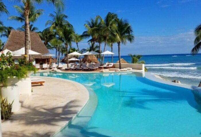Mahekal Beach Front Resort & Spa pool view. Gay-friendly hotel with oceanfront access, palm trees, and lounge chairs for a relaxing vacation.