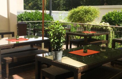 Mainhaus Stadthotel Frankfurt outdoor dining. Gay-friendly hotel's patio area with tables, benches, umbrella, and greenery.