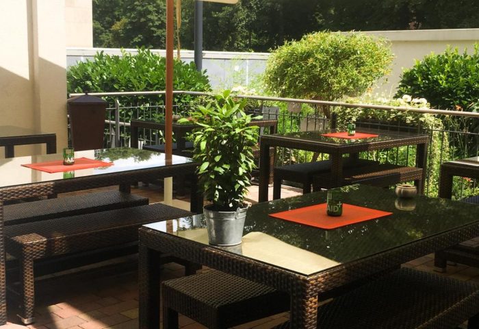 Mainhaus Stadthotel Frankfurt outdoor dining. Gay-friendly hotel's patio area with tables, benches, umbrella, and greenery.