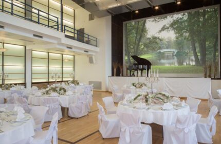 Mainhaus Stadthotel Frankfurt's event space. Gay-friendly hotel with tables set for a celebration. Piano on stage with nature scene.
