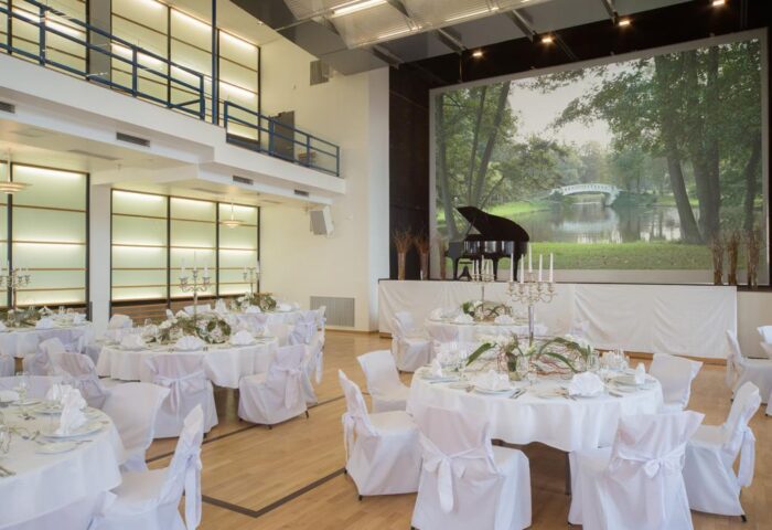 Mainhaus Stadthotel Frankfurt's event space. Gay-friendly hotel with tables set for a celebration. Piano on stage with nature scene.