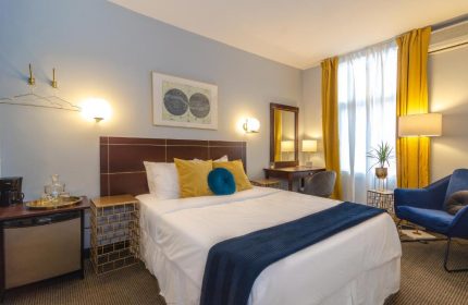 Maison Cartier Montreal gay-friendly hotel room. Queen bed, blue accents, desk, and yellow curtains. Upscale lodging for gay travelers.