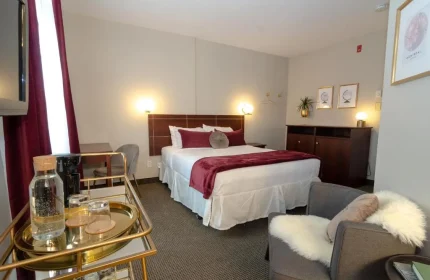 Maison Cartier Montreal gay-friendly hotel room. Bed with burgundy accents, chair with fur throw, and gold bar cart. Upscale, cozy ambiance.