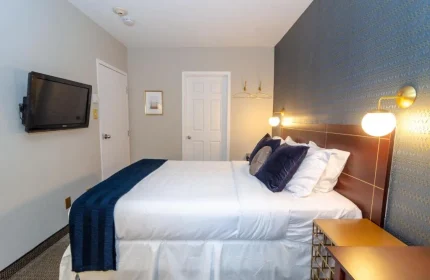 Maison Cartier Montreal gay-friendly hotel room. Bed with white linens, blue pillows, and blue throw. Nightstand and wall-mounted lamps.