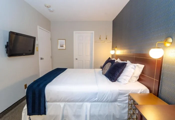 Maison Cartier Montreal gay-friendly hotel room. Bed with white linens, blue pillows, and blue throw. Nightstand and wall-mounted lamps.