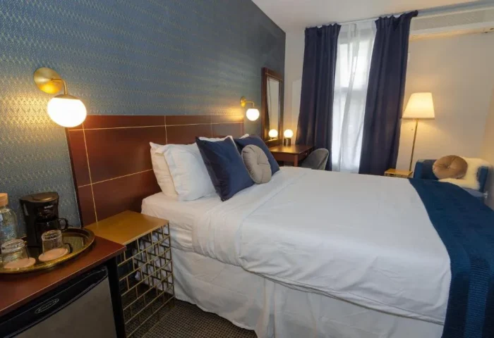 Maison Cartier Montreal gay-friendly hotel room. Queen bed with white linens, blue accents, desk, and lamps. Modern, comfortable lodging.