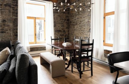 Maison Place Royale interior. Gay-friendly hotel dining area with stone wall, wood table, chairs, bench, and modern chandelier. Luxury In Transit.