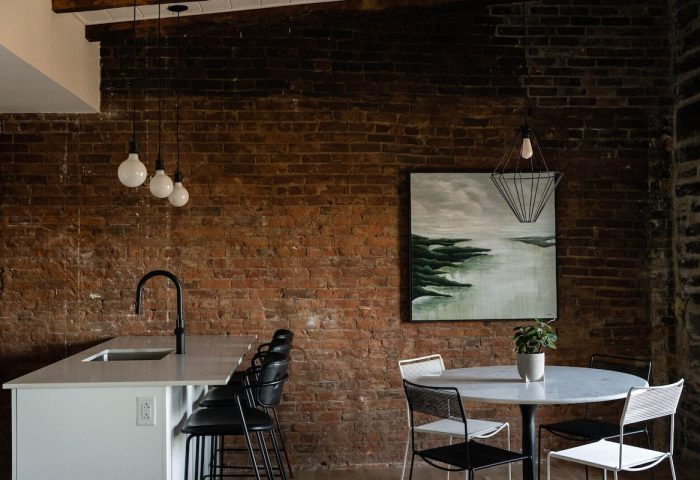 Maison Place Royale interior. Gay-friendly hotel with exposed brick, modern lighting, kitchen island, and dining area. Luxury In Transit travel.