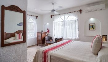 Maison Tulum gay-friendly hotel room. Bright, white interior with bed, mirror, and windows. Comfortable gay travel lodging in Tulum.