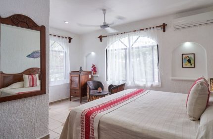Maison Tulum gay-friendly hotel room. Bright, white interior with bed, mirror, and windows. Comfortable gay travel lodging in Tulum.