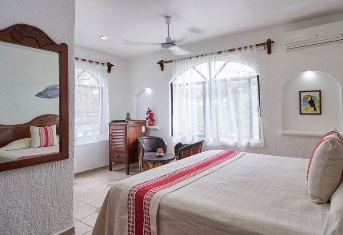 Maison Tulum gay-friendly hotel room. Bright, white interior with bed, mirror, and windows. Comfortable gay travel lodging in Tulum.