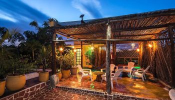 Gay-friendly Maison Tulum hotel rooftop lounge at dusk. Rustic pergola, seating, plants. Relaxing space for gay travelers in Tulum.