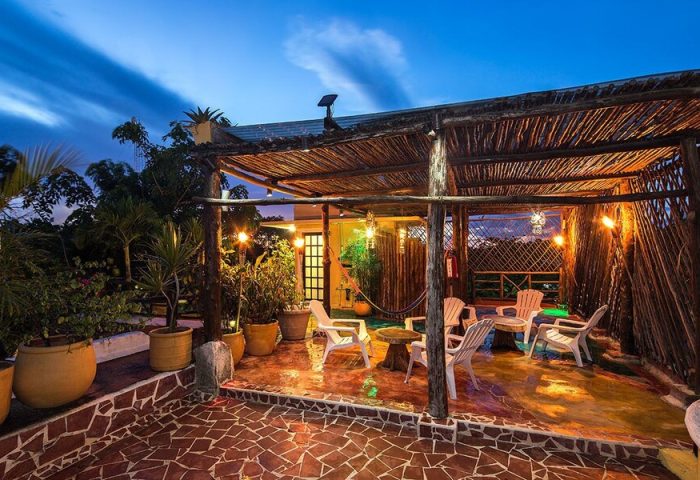 Gay-friendly Maison Tulum hotel rooftop lounge at dusk. Rustic pergola, seating, plants. Relaxing space for gay travelers in Tulum.