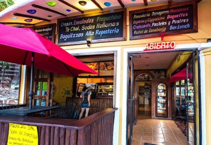 Maison Tulum gay-friendly hotel cafe. Open sign, menu boards, and outdoor seating. Crepes, salads, pastries, and Mexican breakfast options.
