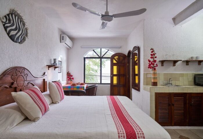 Maison Tulum gay-friendly hotel room. Bed with red accents, kitchenette, zebra art, ceiling fan, window. Gay travel in Tulum, Mexico.