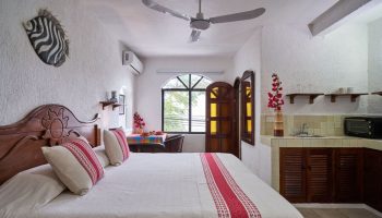 Maison Tulum gay-friendly hotel room. Bed with red accents, kitchenette, zebra art, ceiling fan, window. Gay travel in Tulum, Mexico.