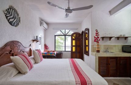 Maison Tulum gay-friendly hotel room. Bed with red accents, kitchenette, zebra art, ceiling fan, window. Gay travel in Tulum, Mexico.