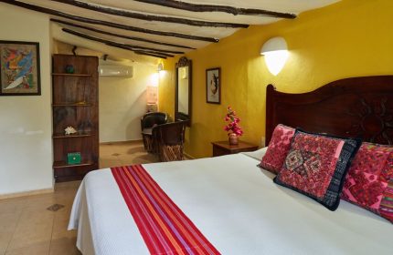 Maison Tulum gay-friendly hotel room. Interior with bed, colorful pillows, yellow wall, and rustic wood accents. Gay travel lodging.