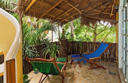 Maison Tulum gay-friendly hotel patio. Tropical getaway with comfy chairs, lush plants, and a thatched roof. Relaxing Tulum vibes.
