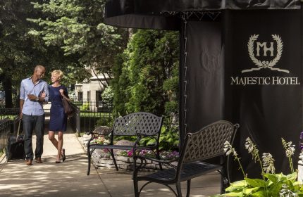 Majestic Hotel Chicago entrance. A gay-friendly hotel featuring a couple arriving with luggage. Benches & flowerbeds adorn the entrance.
