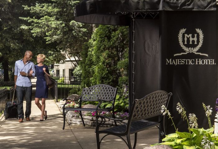 Majestic Hotel Chicago entrance. A gay-friendly hotel featuring a couple arriving with luggage. Benches & flowerbeds adorn the entrance.